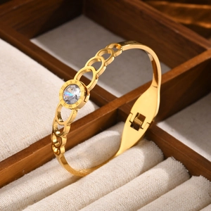 Detailed view of the gold Roman numeral bangle with a central zircon and heart chain detail