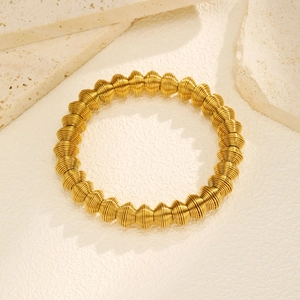 Detailed close-up of golden expandable spring arm cuff on a minimalist stone texture
