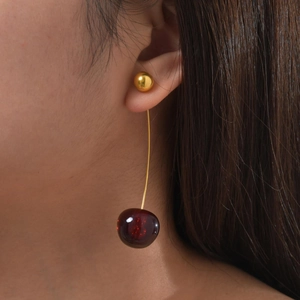 Close-up of elegant cherry dangle earrings with golden bead studs on a model