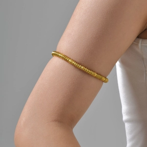 Detail of a flexible gold-plated spring armlet worn on the upper arm with metallic shine