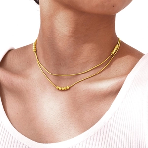 Détail d'un collier double couche doré en maille serpent porté par une femme