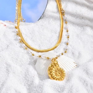 Détail d'un collier doré double épaisseur avec pendentif conque sur fond de plage de sable