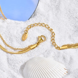Gros plan d'un collier double rang plaqué or 18 carats avec gravure K18 sur sable blanc