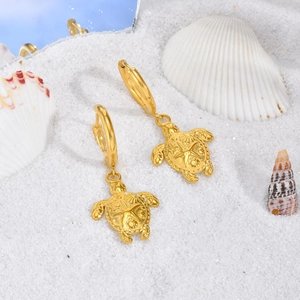 Détail de boucle d'oreille tortue plaquée or 18 carats sur sable blanc et coquillages