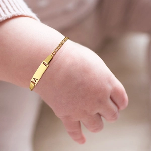 Detailed view of an 18k gold plated baby ID bracelet with hollow letters on Figaro chain
