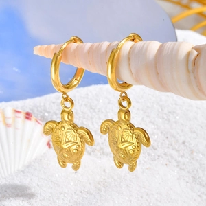 Boucles d'oreilles créoles tortue en acier doré 18K sur un coquillage et sable blanc