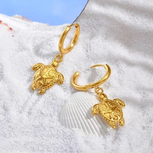 Gros plan de boucles d'oreilles tortue en or 18 carats sur sable blanc fin