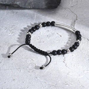 Macro detail of men's matte black beaded bracelet with adjustable woven cord and curved silver tube