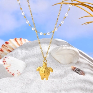 Collier tortue de mer dorée avec perles blanches sur sable de plage et coquillages