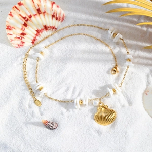 Detail of a gold ocean necklace featuring white shell square and pearl on a beach background