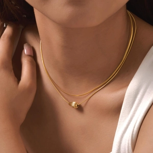 Detail showing dual-layer gold plated necklace with a textured oval drop pendant on model