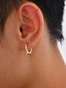 Nahaufnahme eines goldenen Edelstahl-Ohrrings mit scharfen Nieten im Punk-Stil für Herren