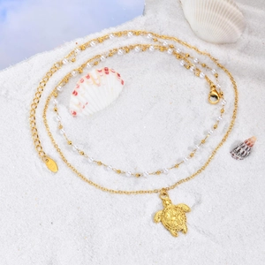 Détail du pendentif tortue de mer dorée et perles sur sable blanc avec poinçon K18