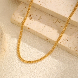 Close-up of 18K gold double layer bead chain necklace on a beige travertine stone