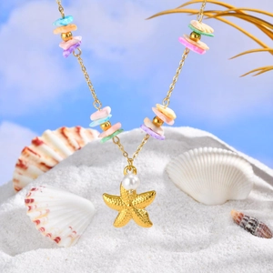 Detail of a golden starfish pendant with a white pearl and colorful shell beads on sand