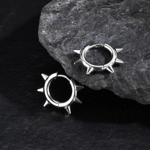 Nahaufnahme der polierten Edelstahl-Creolen im Punk-Stil mit Spikes auf schwarzem Stein