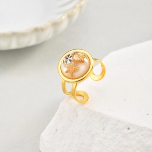 Golden adjustable ring with starfish and seashell resin inlay on a white stone background