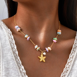 Detail of golden starfish pendant and shell beads necklace on a white lace top