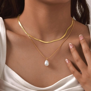 Detail of double-layer gold snake chain necklace with a drop pearl pendant on model