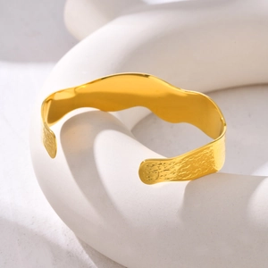 Detail of golden C-shaped wave cuff bangle with hammered texture and polished finish