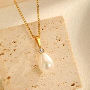 Close-up of a gold waterdrop pearl pendant necklace with sparkling zircon on a textured stone