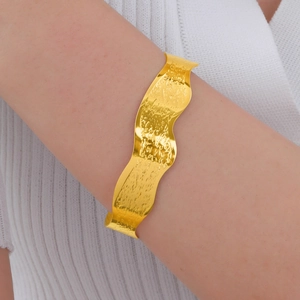 Detail of gold water ripple cuff bracelet showing hammered texture on model wrist