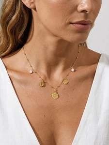 Gros plan du collier en or 18K avec perles et breloques marines sur un mannequin en lin