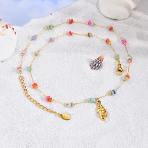 Golden sea shell necklace with colorful beads on a white sandy beach background