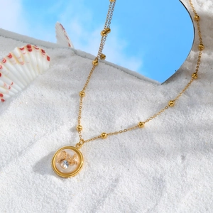 Detail of golden starfish and seashell resin pendant necklace on a sandy beach setting