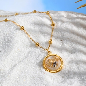 Detailed close-up of golden ocean necklace with shell and starfish on white beach sand