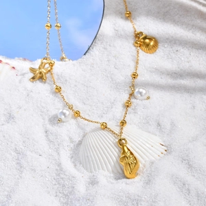 Détails macro des pendentifs étoile de mer et coquillage en or 18K avec perles sur sable