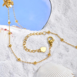 Bracelet de cheville doré perlé avec breloque cœur sur sable blanc et coquillage