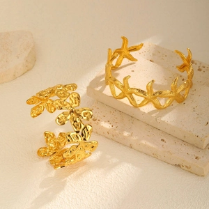 Gold-plated starfish and floral textured open cuff bracelets on a beige stone stand
