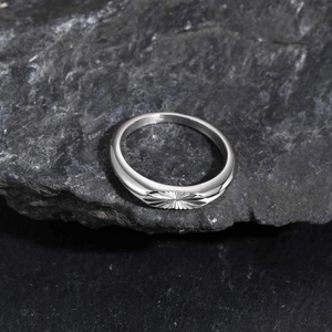 Polished silver stainless steel ring with starburst pattern on grey rock surface