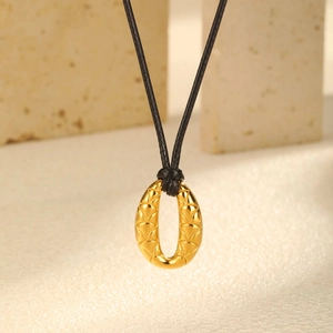 Macro view of golden oval pendant with 3D triangle texture on black cord necklace