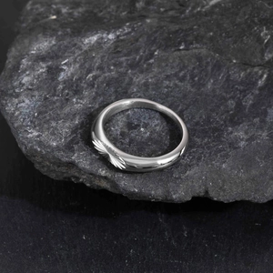 Macro view of men's stainless steel ring with radial textures on black rock