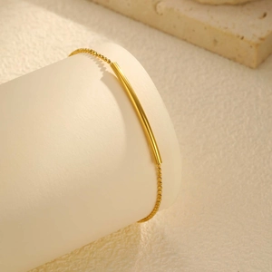 Détail de perles facettées en or 18K et tube incurvé sur un bracelet minimaliste