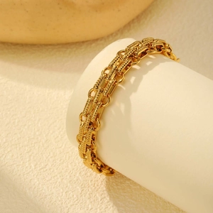 Layered gold stainless steel bracelet with textured rectangular links on a display stand