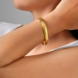 Polished 18K gold plated stainless steel bangle with hidden clasp on model's wrist