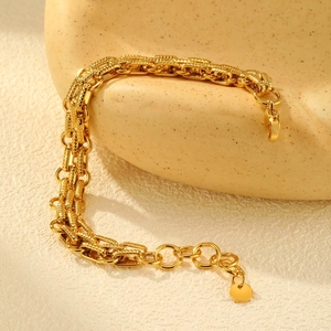 Detail of a multi-layer gold chain bracelet with lobster clasp on a beige textured stand