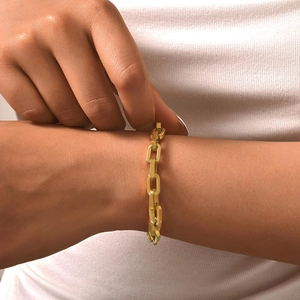 Close-up of a gold paperclip link chain bracelet worn on a woman's wrist over white knitwear