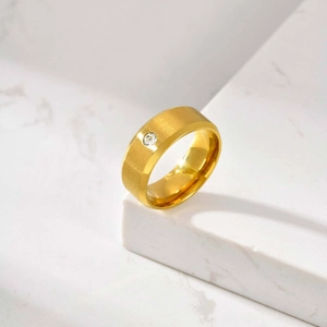 Vue détaillée d'une bague dorée mate avec diamant central sur un fond de marbre blanc