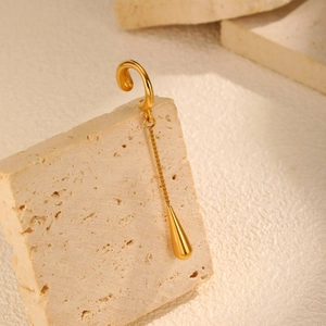 Detailed view of golden teardrop pendant earring on textured stone surface background