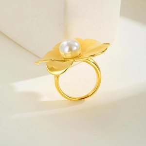 Gros plan d'une bague fleur dorée élégante avec perle blanche sur socle blanc