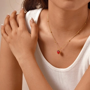 Gros plan d'une chaîne dorée avec pendentif cœur rouge portée par un mannequin