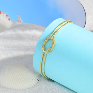 Detailed view of golden knotted snake chain anklet on blue stand with white sand and shells