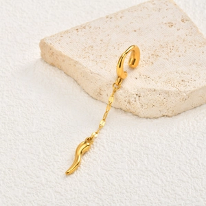 Detail of a gold chili charm ear cuff with chain on a textured stone background
