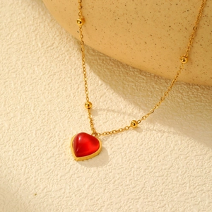 Gros plan d'une chaîne à billes dorée avec pendentif cœur rouge sur pierre texturée