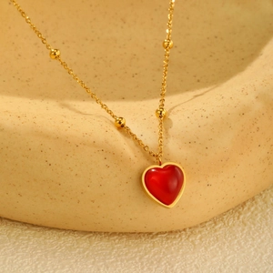 Détail du collier à perles dorées avec pendentif cœur rouge sur plateau céramique