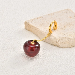 Detail of a red cherry-shaped earring with golden chain on a natural stone base